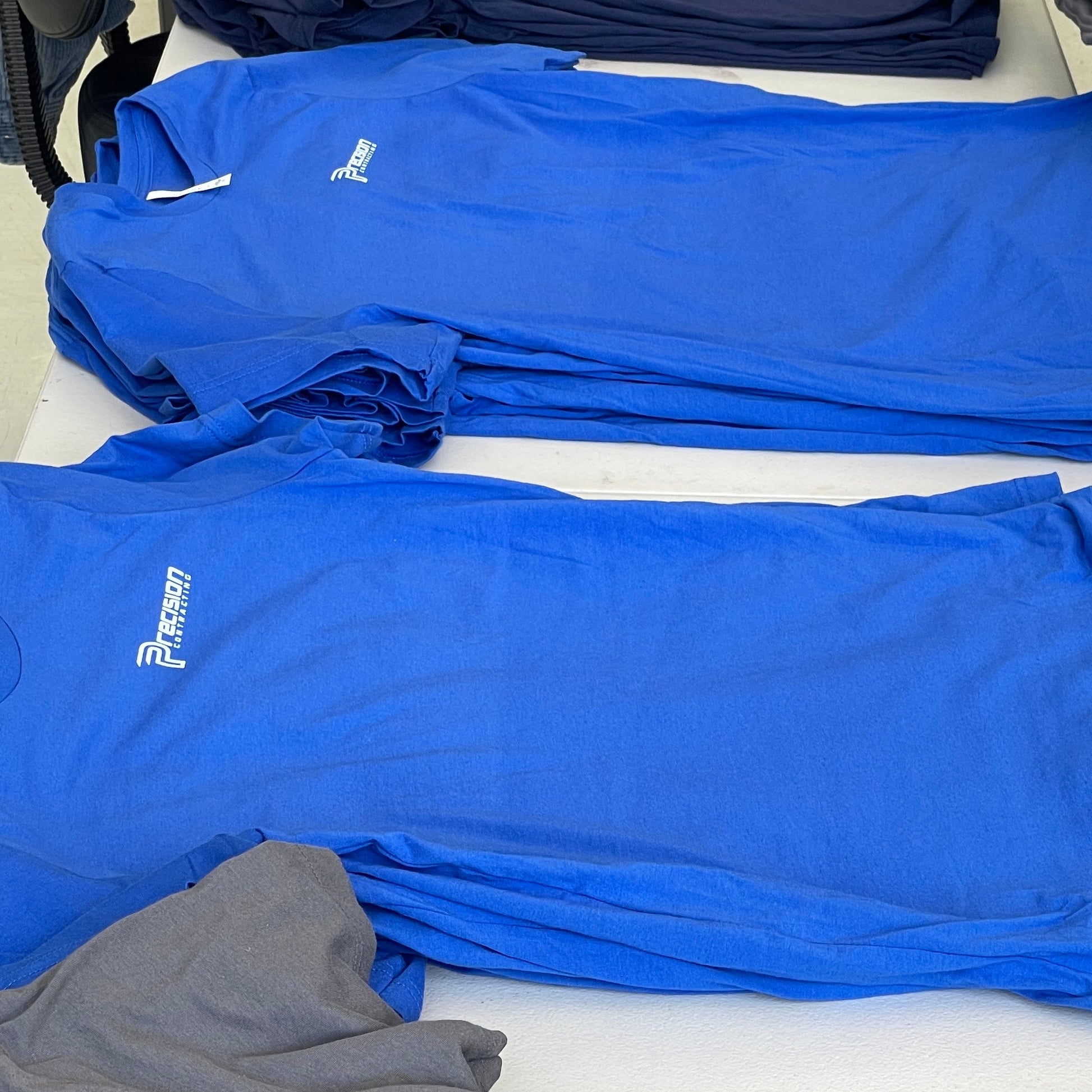 Stacks of blue and gray shirts with a brand logo on a white surface.