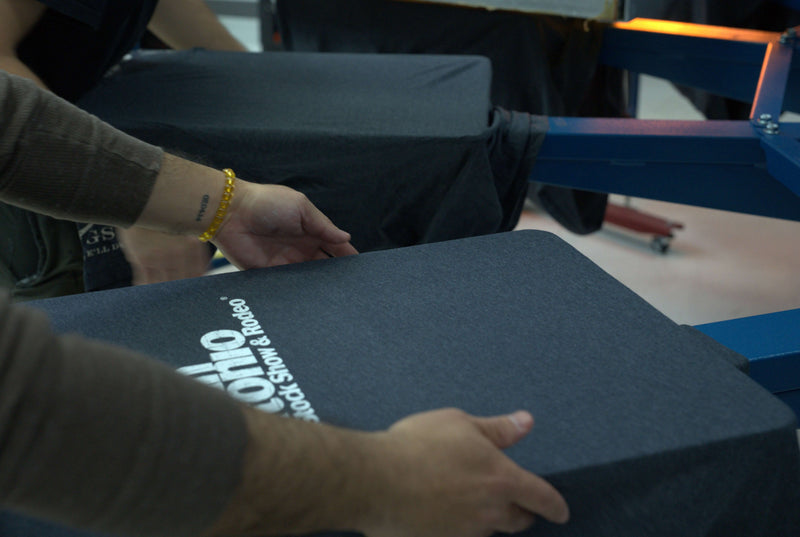 A screen printing operator pulling a finalized shirt from the machine after the shirt has been painted