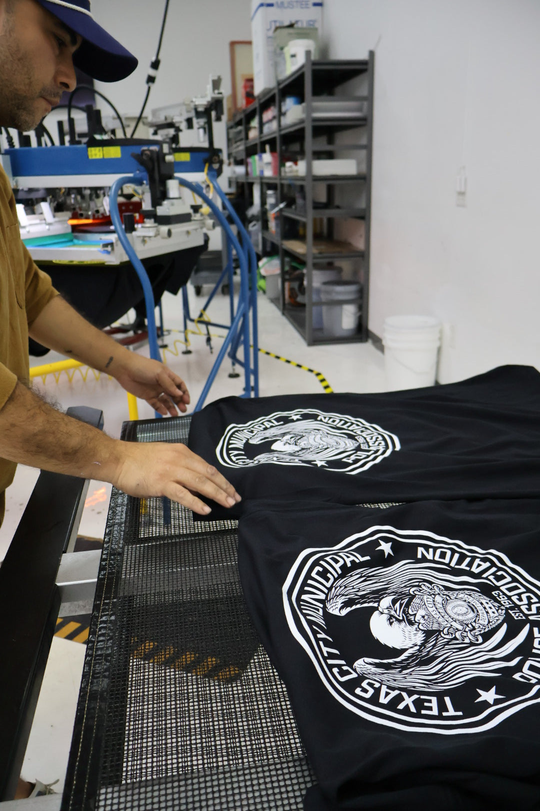 Person holding a black t-shirt with white graphics and text in an industrial setting.